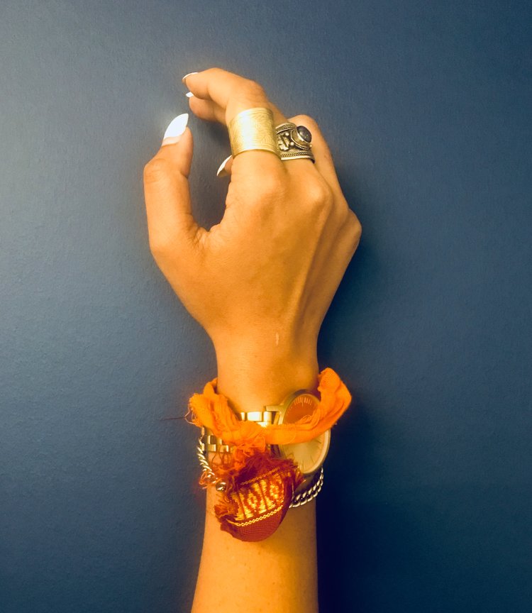 two dark-skinned arms with a variety of bracelets on them including a orange fabric writst tie